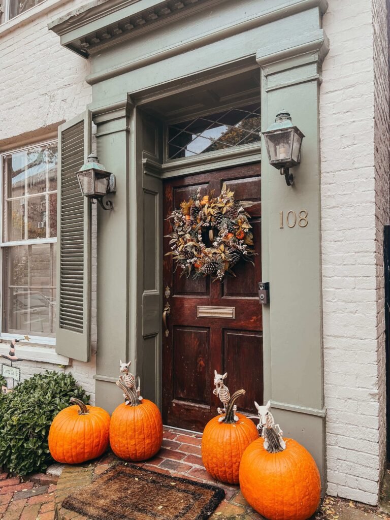 Outdoor Halloween decor idea with a fall wreath, pumpkins, and skeleton creatures on the porch